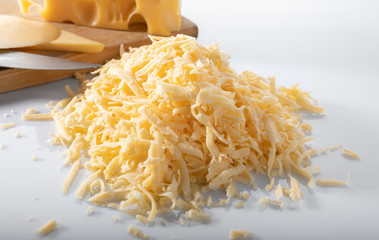 Grated Swiss cheese, wooden board and a knife on white background