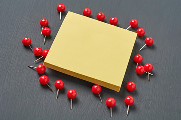Scattered many red push pins near square blank paper lies on dark concrete desk in office, school or home. Space for text. Close-up