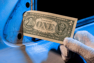 A male hand in a white glove holds one dollar bill instead of a mirror on the car door. Poverty and...