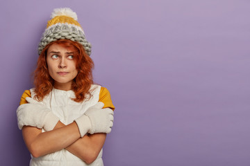 Beautiful redhead woman in wool knitted hat, white gloves and vest, crossed arms over body,...