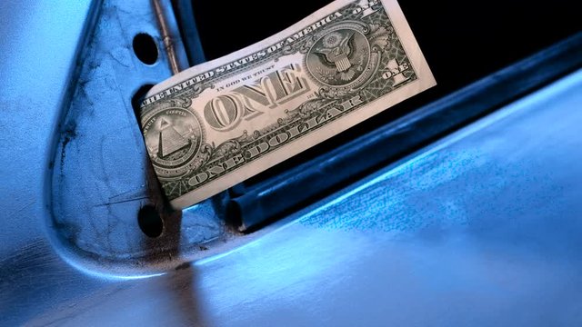 A male hand in a white glove inserts one dollar bill instead of a mirror on the car door. Blue tone. Poverty and cheap wages in the automotive service center. Low paid wage labor. A scratched metal.