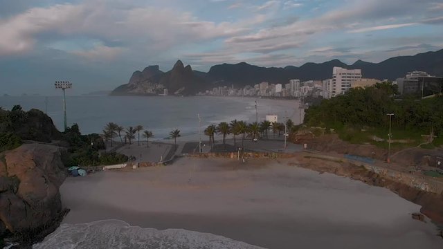 Aerial slow motion backing off revealing the ocean waves that come in on Devils beach at the Arpoador in Rio de Janeiro with Ipanema and Leblon in the background at early morning sunrise