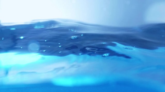The clean water surface in slow motion fills the screen with water splashing shop the water drop and waving liquid surface with an air bubble. 1080p 29.97fps