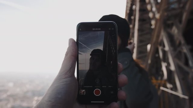 Smartphone in male hand is filming a romantic portrait of happy smiling woman posing on top of Eiffel Tower slow motion.