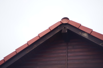 Part of the pediment of a wooden house with a red rooftop metal tile.
