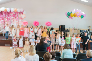 Obraz na płótnie Canvas Children's party in primary school. Young children on stage in kindergarten appear in front parents. blurry