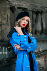A blonde in a blue cloak walks along the street against the background of buildings