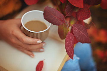 A book, a glass of coffee and a bouquet of autumn leaves on his lap