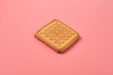 One whole square cookie lies on pink desk on kitchen. Close-up