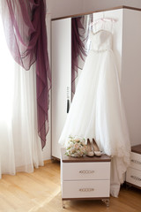 Bridal accessories: wedding dress, shoes and bride's bouquet in a loght room. Bride's room in wedding day