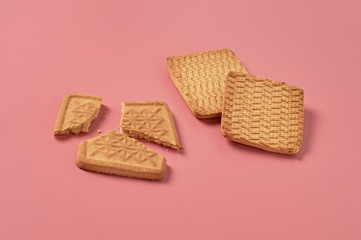 Whole and broken square cookies lies on pink desk on kitchen. Close-up