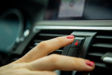 a female finger press the emergency light button on the dashboard of a car. close-up, soft focus, in the background car interior details in blur, side view