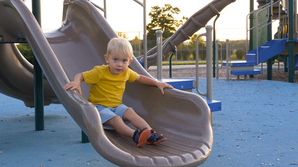 Little boy (toddler, two years old kid) having fun, sliding down. Outdoor plastic playground slide...