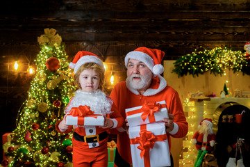 Santa Claus and little boy holds Christmas present. Christmas, family holidays and childhood. Little child with Santa Claus and Christmas gift at home. Kid boy and father in Santa costume and beard.