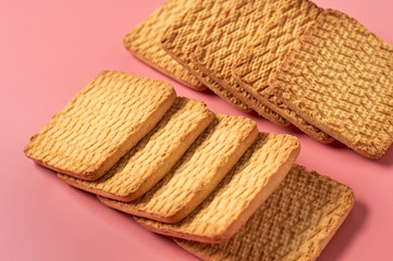 Two heaps of whole square cookies lies on pink desk on kitchen. Close-up