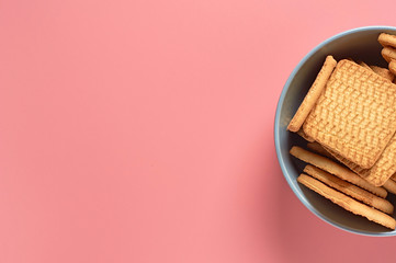 Gray bowl full of whole square cookies lies on pink desk on kitchen. Space for text. Top view