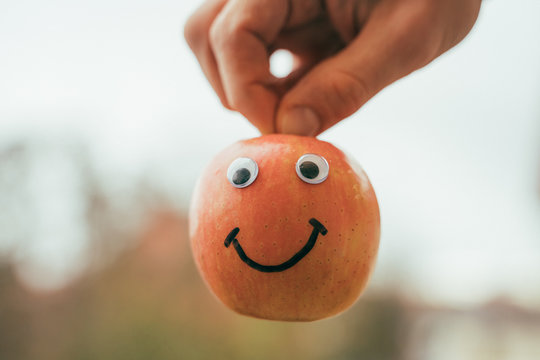 Ein fr&ouml;licher Apfel wird von einer Hand am Stiel gehalten