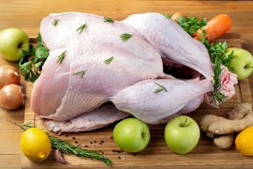 Whole raw turkey on wooden cutting board with apples and vegetables,