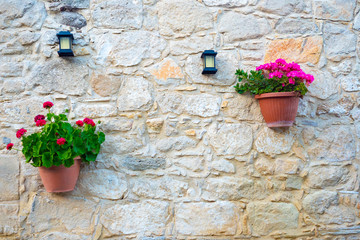 Fototapeta na wymiar Cyprus. Kuklia. The wall of the building is made of shell. The wall is decorated with flowers and lanterns. Pelargonium in pots. Background of yellow stones. Decoration of the facade of the house.