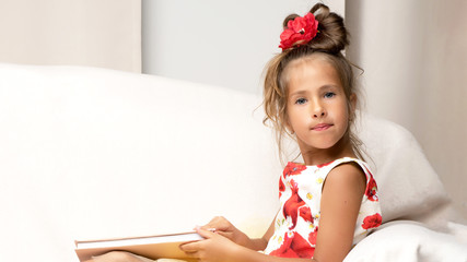 A little girl is sitting on the couch and reading a book.