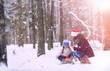 A winter fairy tale in the forest. A girl on a sled with gifts on the eve of the new year in the park. Two sisters walk in a New Year's park and ride a sled with gifts.