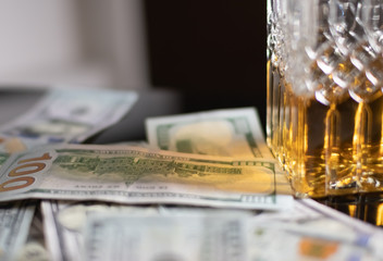Hundred dollar bills are scattered on the table next to a crystal decanter filled with whiskey. On a black glass table