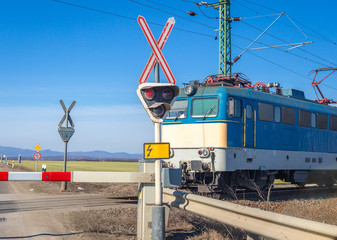 Red traffic light, lowered barrier, approaching electric train