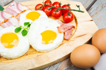 Tasty fried eggs with vegetables on a wooden plate.