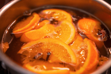 Making hot alcoholic mulled wine with oranges and spices. Christmas beverages boil in the metal pan. Glintwine from rose wine with citrus, cloves, star anise, cinnamon.