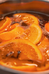 Making hot alcoholic mulled wine with oranges and spices. Christmas beverages boil in the metal pan. Glintwine from rose wine with citrus, cloves, star anise, cinnamon.