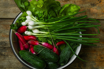 Fresh vegetables cucumbers, green onions, radish and green salad in a white dish placed on an old wooden table top view