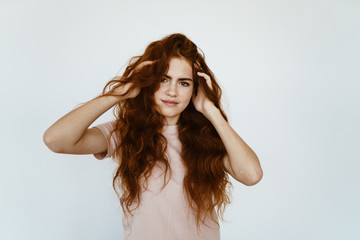 a teenage girl, capriciously wrinkled her forehead and fingering her luxurious hair, expressing displeasure. gray background