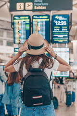 the tourist at the airport looks at the scoreboard, standing with his back to the camera, a backpack behind his shoulders, a hat on his head