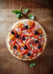 Pizza with ham, cherry tomatoes, mozzarella cheese, black olives and fresh basil. Rustic wooden background. Top view.
