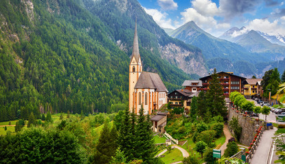 Heiligenblut, Austria. Panoramic aerial view of Saint Vincent Church, famous tourist attraction in East Tyrol region in Alps. Grossglockner Mountain landscape with high snowbound summits. - obrazy, fototapety, plakaty