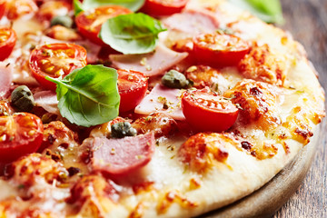  Tasty pizza with ham, cherry tomatoes, mozzarella cheese, capers and fresh basil on wooden background. 