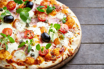 Tasty pizza with cherry tomatoes, black olives, mozzarella cheese and fresh oregano. Brown wooden background.  Close up.