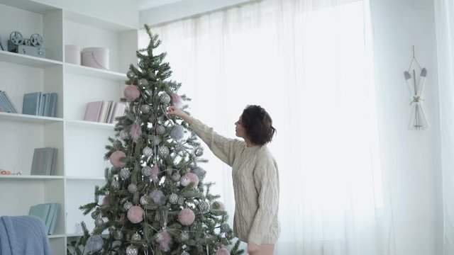 Pretty woman decorates Christmas tree in cozy light room