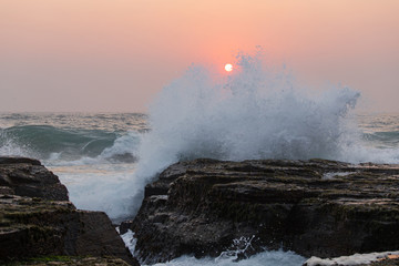 Fototapeta premium A wave crash into the rocks with sun on the background.