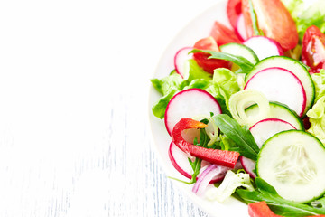 Healthy salad with tomatoes, cucumber, radish, lettuce and rocket. Bright background. Close up.