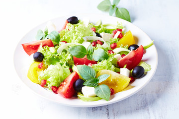  Healthy salad with pomegranate seeds, tomatoes, black olives, lettuce and fresh herbs. Bright background. Close up.