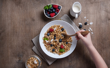 sweet muesli with berries in plate with milk on wooden table.