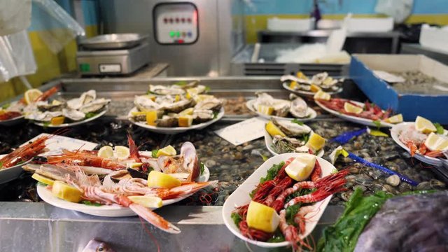 Traditional fish market counter full of prepared portions of different types of seafood. Fresh oysters, shrimps and shellfishes lying on plates inside the ice. Luxury market counter