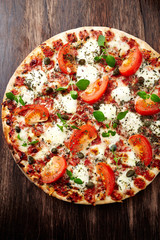 Pizza with tomatoes, mozzarella cheese and fresh herbs. Home made food. Concept for a tasty and hearty meal. Brown wooden background. Top view. 