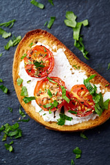 Crostini withe cream cheese, cherry tomatoes and fresh basil. Dark stone background. Close up. Top view. 