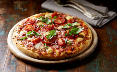 Pizza with cherry tomatoes and fresh herbs. Home made food. Concept for a tasty and hearty meal. Brown wooden background. 