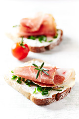 Tasty sandwiches with cream cheese, smoked ham, cherry tomatoes and fresh herbs. Bright wooden background. Close up. 