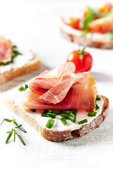 Tasty sandwiches with cream cheese, smoked ham, cherry tomatoes and fresh herbs. Bright wooden background. Close up. 