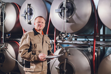 Mature man examining the quality of craft beer at brewery. Inspector working at alcohol manufacturing factory checking beer. Man in distillery checking quality control of draught beer.