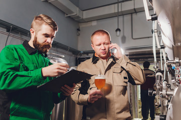 Mature man examining the quality of craft beer at brewery. Inspector working at alcohol manufacturing factory checking beer. Man in distillery checking quality control of draught beer.